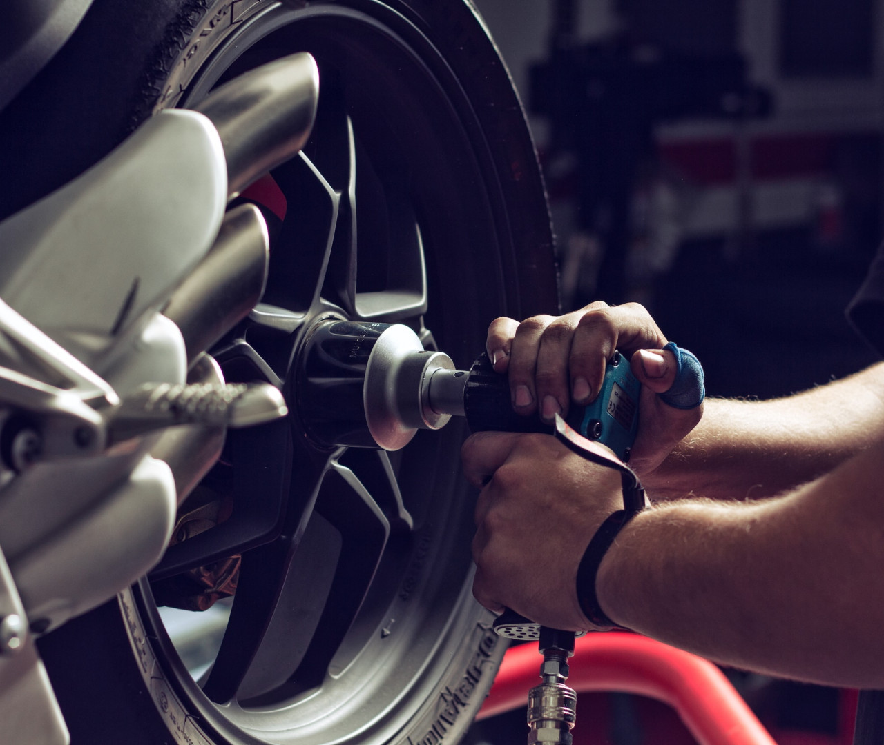 Nahaufnahme eines Mechanikers, der mit einem Präzisionswerkzeug an der Felge eines Motorrads arbeitet. Die Hände führen mit einem türkisfarbenen Werkzeug sorgfältige Einstellungen an der silbernen Speichenfelge durch. Professioneller Reifenservice in der Motorradwerkstatt.