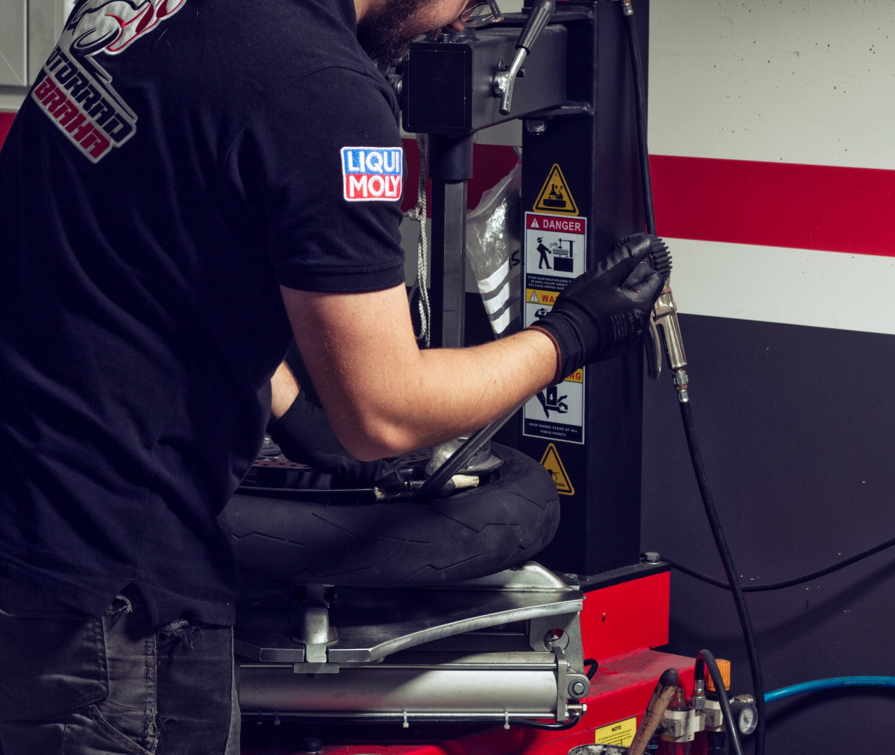Motorradtechniker mit schwarzen Handschuhen und einem LIQUI MOLY-Shirt bei der Arbeit an einem Reifen mit einer professionellen Reifenmontagemaschine in einer Werkstatt.