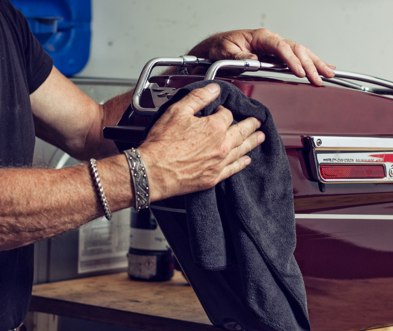 Handwerker poliert sorgsam mit einem dunklen Tuch einen burgunderroten Vintage-Gegenstand mit verchromten Beschlägen, vermutlich Teil eines klassischen Motorrads oder speziellen Koffers.